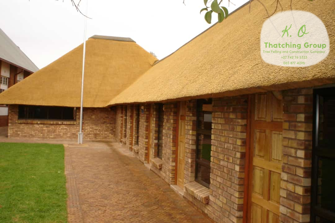 Face-brick lodge veranda under a long golden thatch roof with timber doors