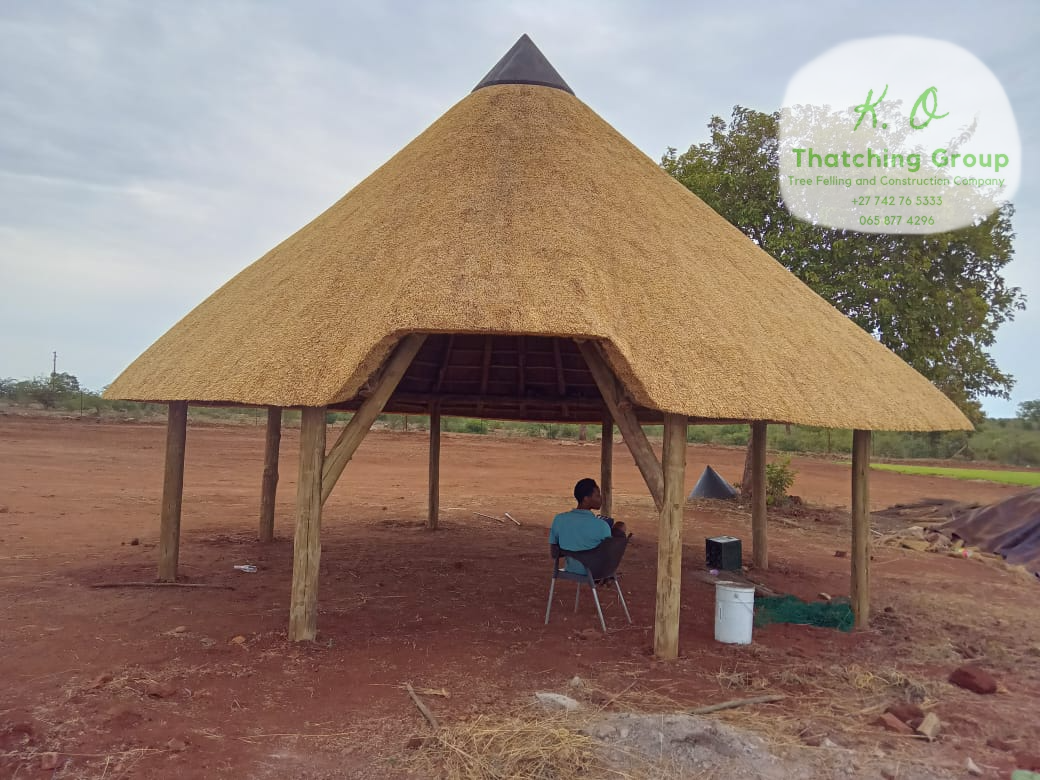 Open-sided conical thatched shelter built on timber poles in a red-earth landscape
