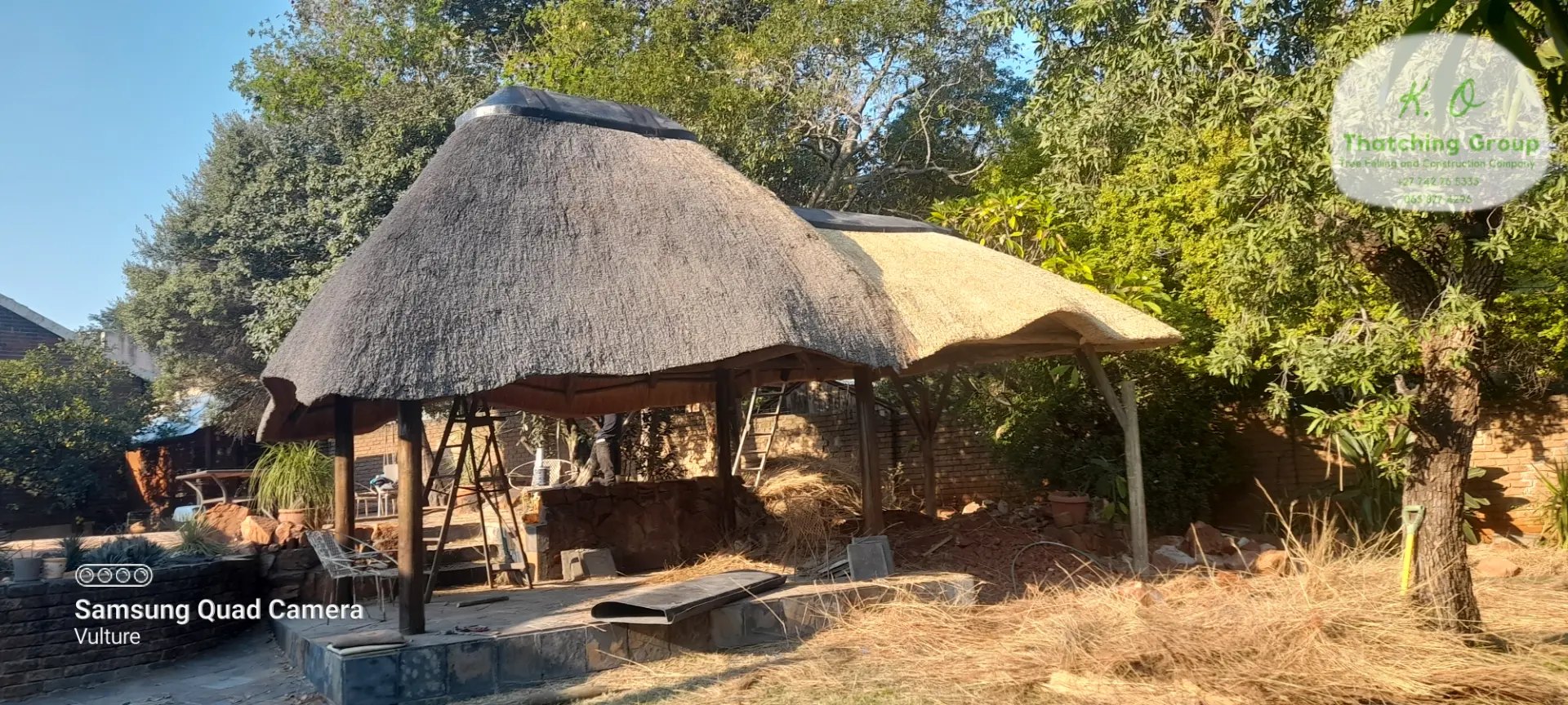 Two-tone thatched gazebo in a landscaped garden, part-way through re-thatching